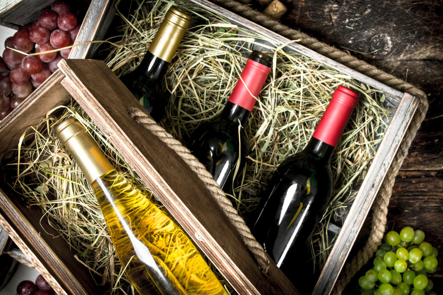 Weinflaschen in Holzkiste mit Stroh, daneben Trauben. Weinflaschen in Holzkiste mit Stroh, daneben Trauben.